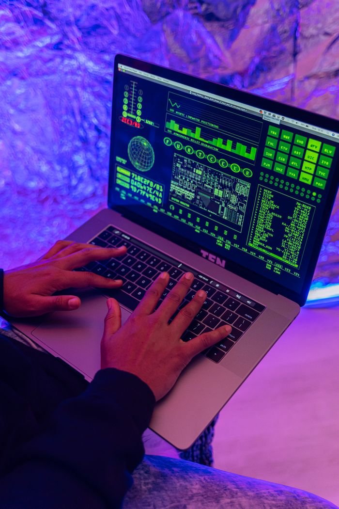 Close-up of hands typing on a laptop displaying green code, indoors, purple lighting.